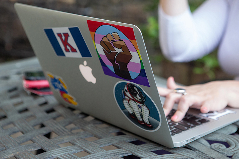 Closeup of laptop with diverse stickers on it while female student types on keyboard.