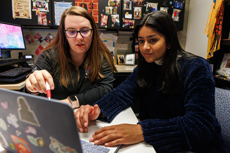 Two diverse young women work together off of a laptop.